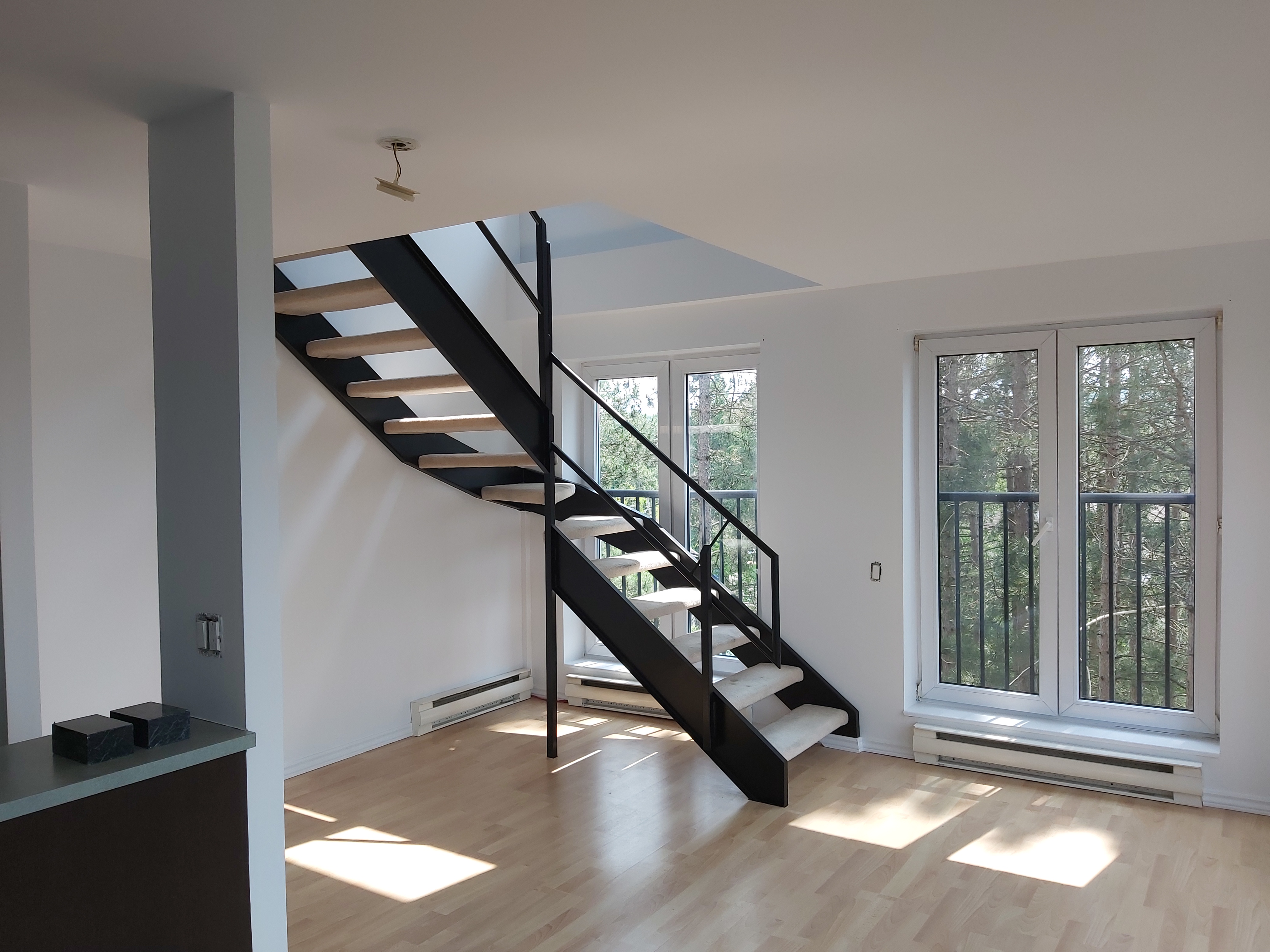 Elegant living room with large windows and staircase, completely refinished and repainted with a refined, high-quality finish.